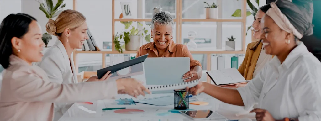 Diverse group of women collaborating and laughing around an office table